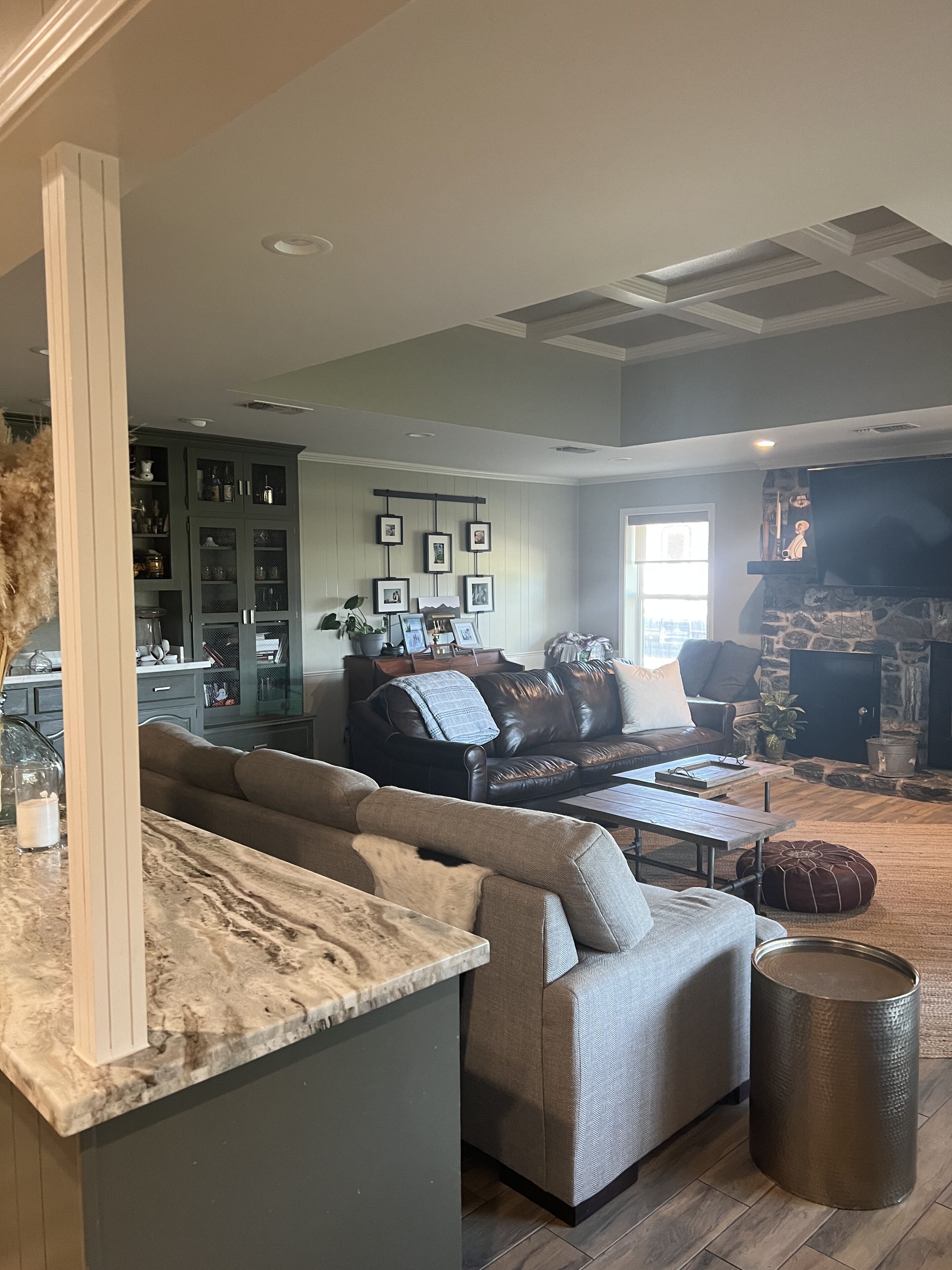 A spacious living room with a large sectional sofa, a fireplace, and a kitchen area with a marble countertop.