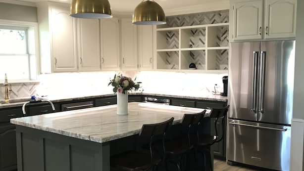 Una cocina con una isla central, taburetes de bar, un refrigerador de acero inoxidable e iluminación colgante.