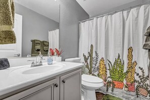 A bathroom with a white sink, toilet, and shower curtain featuring a cactus design. - Modern desert vibes in the heart of Gilbert! (Gilbert)