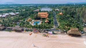 A resort with a swimming pool, beach, and thatched-roof structures.