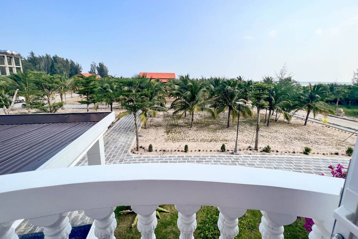 A balcony with a view of a sandy area with palm trees and a paved walkway.