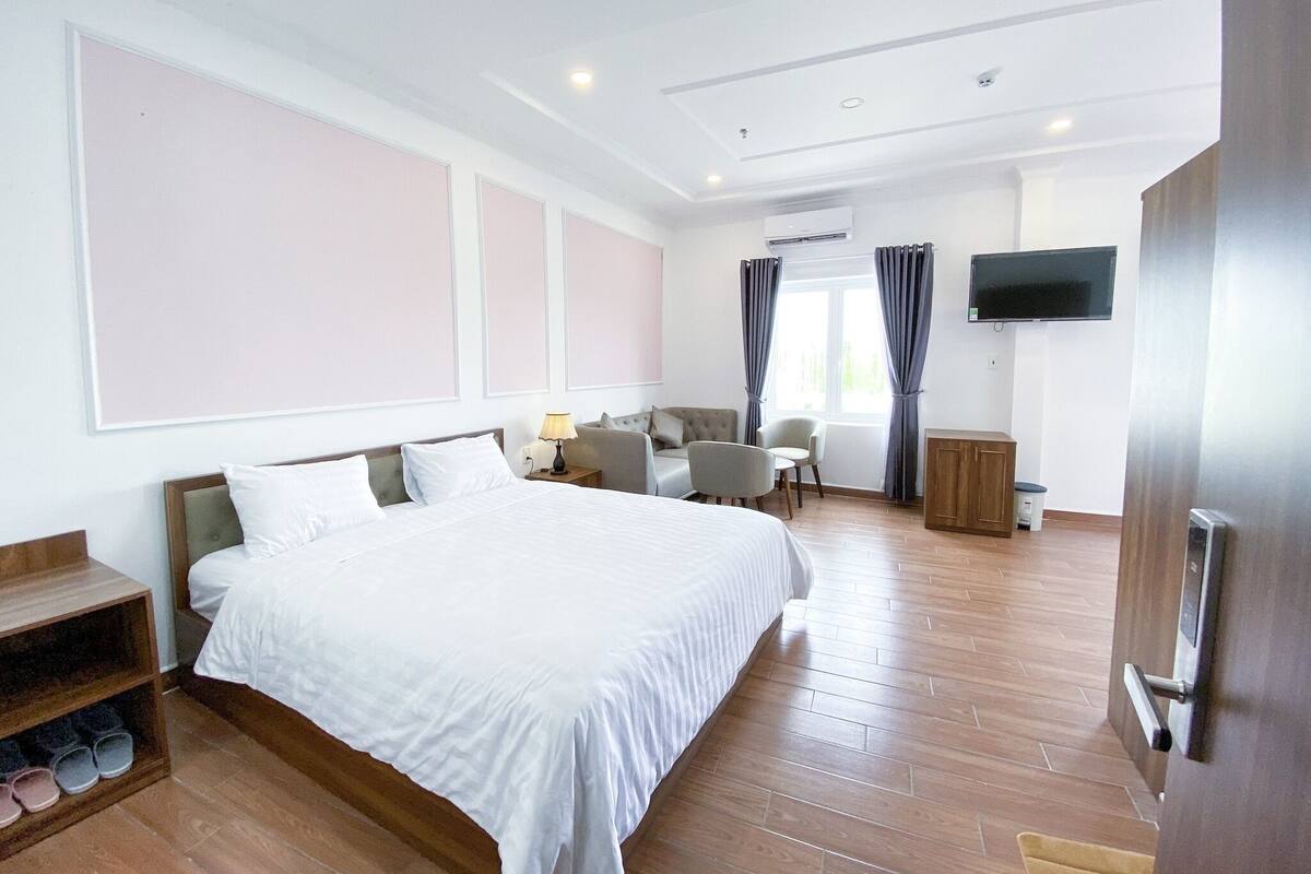 A hotel room with a large bed, a desk, a chair, a TV, and a wardrobe.