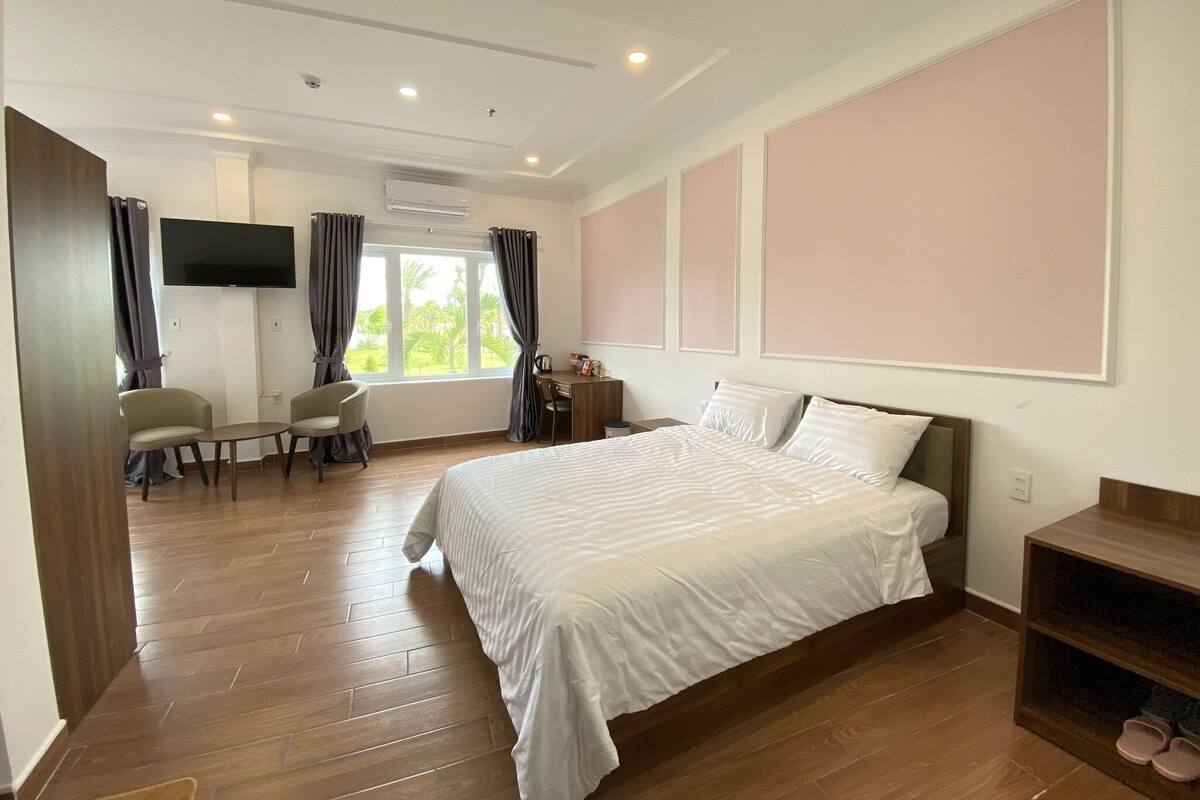 A hotel room with a large bed, a desk, a chair, a TV, and a window with curtains.
