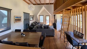 Een ruime woonkamer met een hoge plafond, een eettafel en een zithoek.