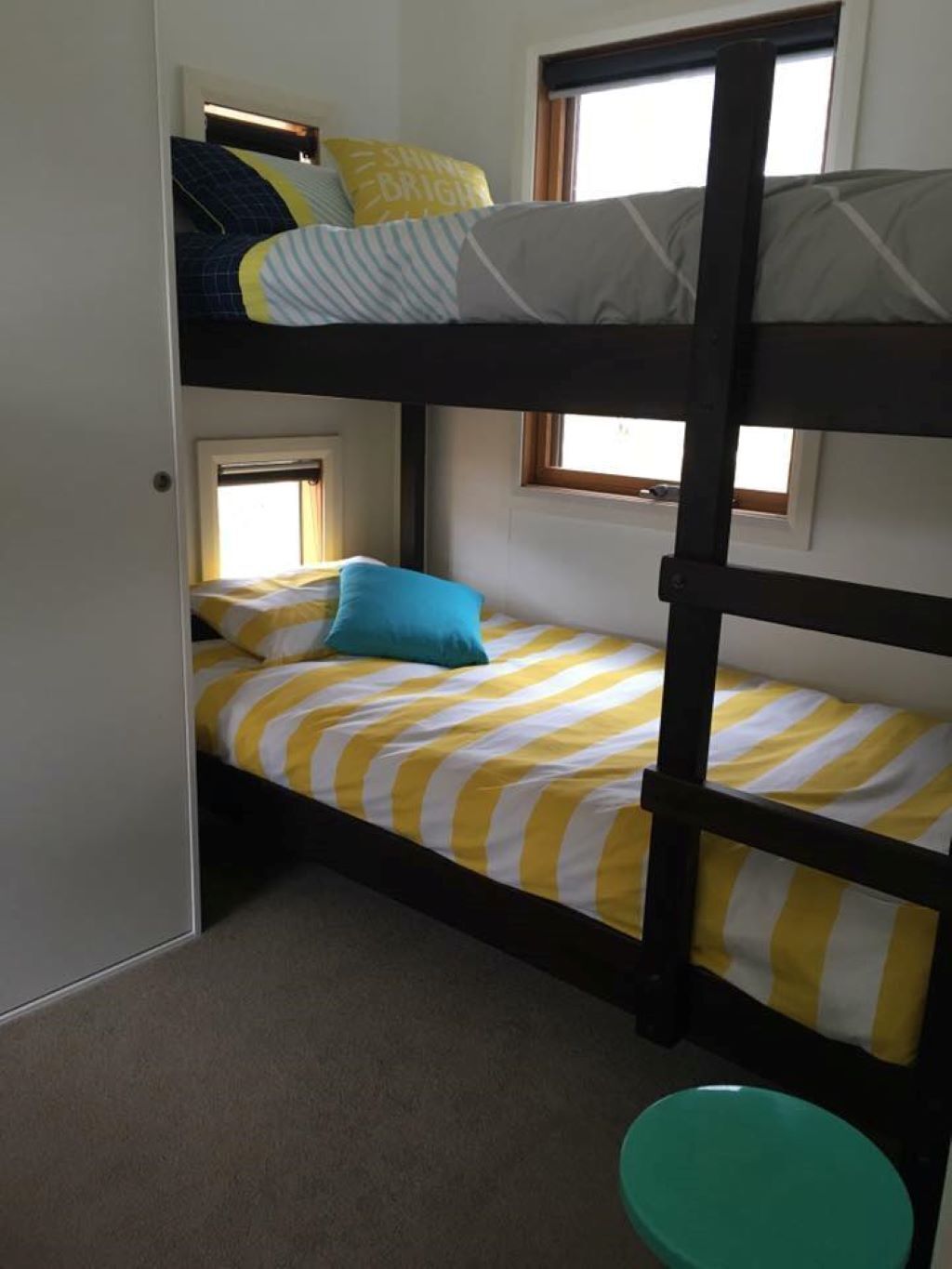 A bunk bed room with striped bedding, a teal bucket, and a window with curtains.
