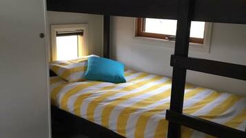 A bunk bed room with striped bedding, a teal bucket, and a window with curtains.