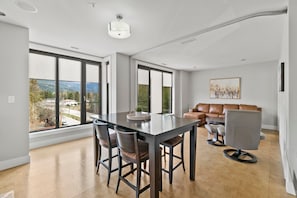 Ampla sala de estar com uma grande mesa de jantar, assentos confortáveis e janelas grandes que oferecem vista para o exterior.