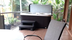 A hot tub on a balcony with steps leading up to it, surrounded by greenery.