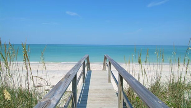 A wooden boardwalk leading to a beach with clear blue water and sandy shore.