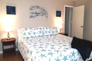 A bedroom with a bed featuring a star pattern, two bedside tables with lamps, and a door leading to another room. - Palm Gardens - Hot Tub - Screened Patio - Minutes to the Beach - Pets (Venice)