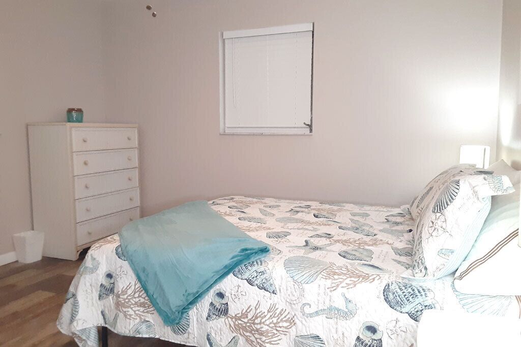 A bedroom with a bed, a dresser, a window, and a wall-mounted light.