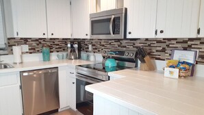 A modern kitchen with white cabinets, a stainless steel dishwasher, a microwave, a stove, and a coffee maker.