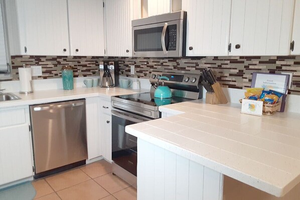 A modern kitchen with white cabinets, a stainless steel dishwasher, a microwave, a stove, and a coffee maker. - Palm Gardens - Hot Tub - Screened Patio - Minutes to the Beach - Pets (Venice)