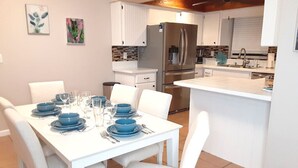 A modern kitchen with white cabinetry, a stainless steel refrigerator, and a dining area with a white table set for four.