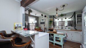 A kitchen with a marble countertop, wooden chairs, a light blue cabinet, and a hanging light fixture.