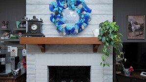 A fireplace with a blue and white wreath, a clock, and a plant.