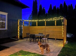 Une terrasse avec une clôture en bois, des guirlandes lumineuses et une table entourée de chaises.
