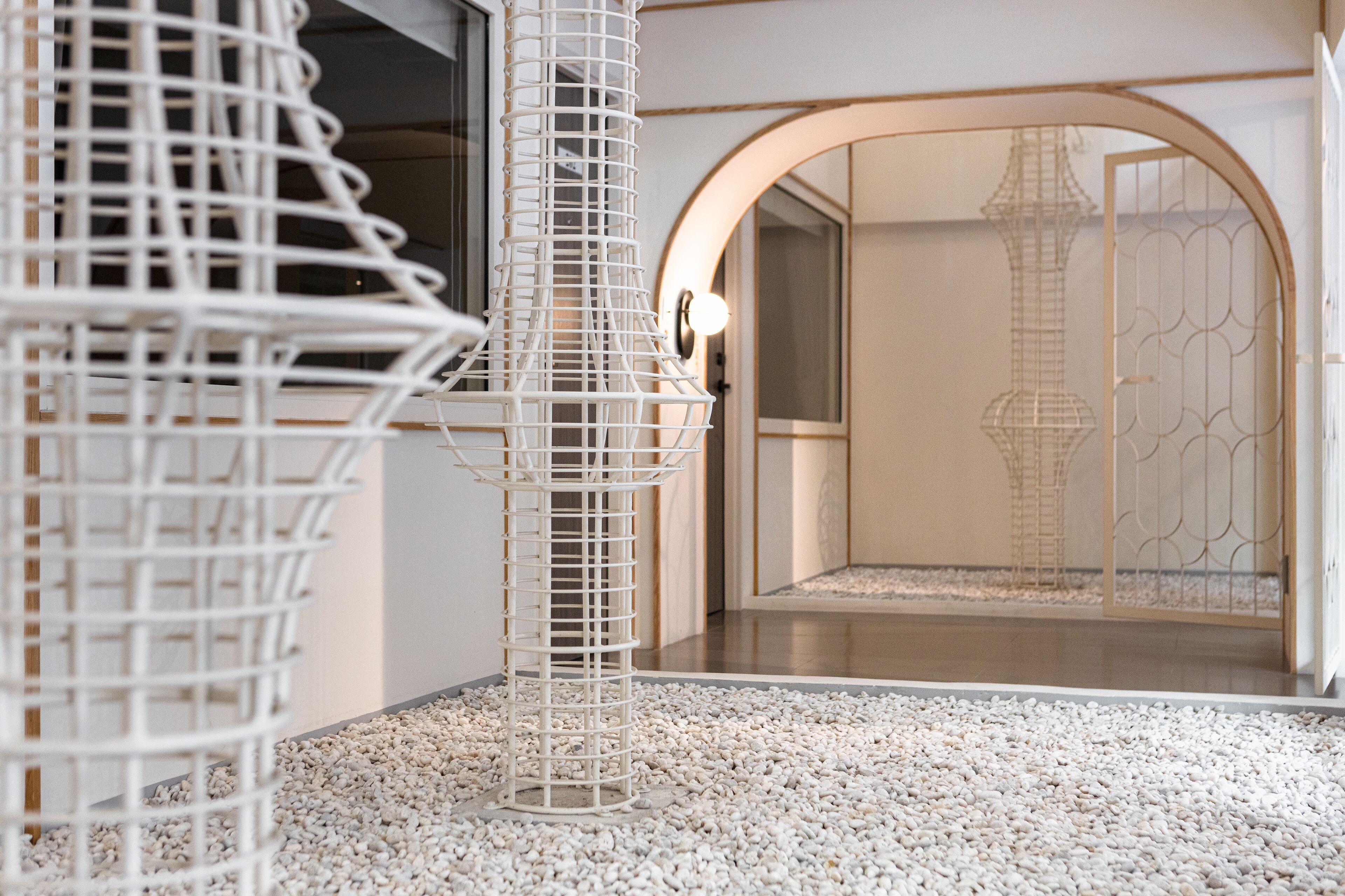 A modern interior with a white spiral structure, a pebbled floor, and a doorway leading to a room with a patterned door.