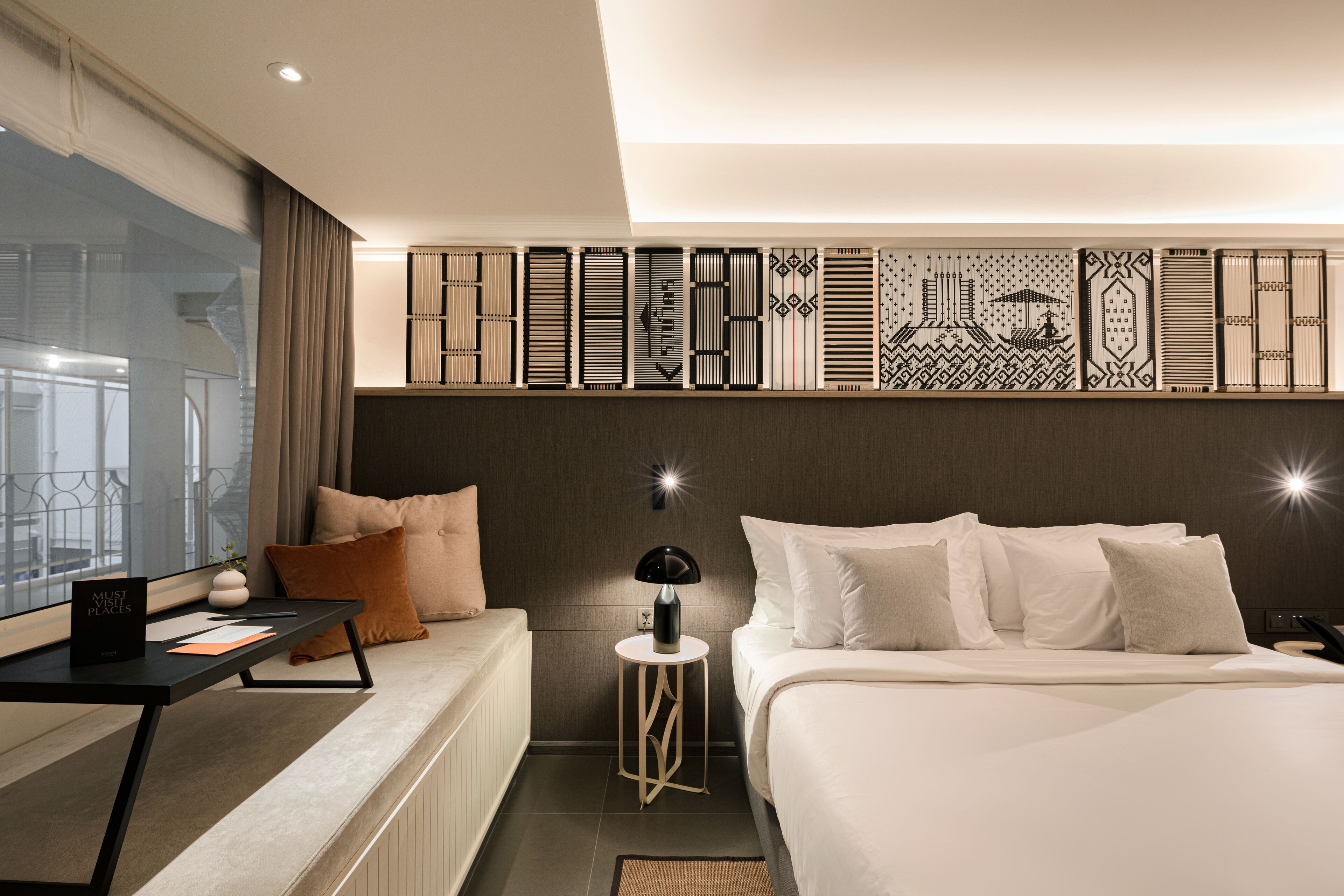 A modern hotel room with a large bed, a bedside table, a small side table, and a decorative wall panel.