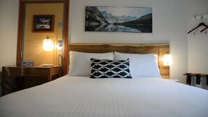 Ein Hotelzimmer mit einem großen Bett, einem Holzkopfteil, zwei Nachttischlampen, einem gerahmten Bild an der Wand und einem Schreibtisch mit Lampe.