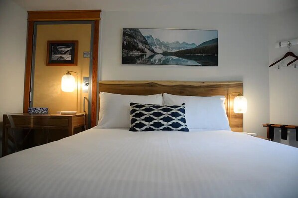 A hotel room with a large bed, wooden headboard, two bedside lamps, a framed picture on the wall, and a desk with a lamp. - Cozy 1Bed/1BA Hotel Room/AC/UG Parking/Gym (Canmore)