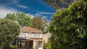 Una casa a due piani con piscina, circondata da vegetazione rigogliosa e alberi.