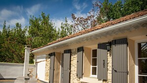 Un edificio in pietra con patio piastrellato, finestre con persiane e un muro in pietra.