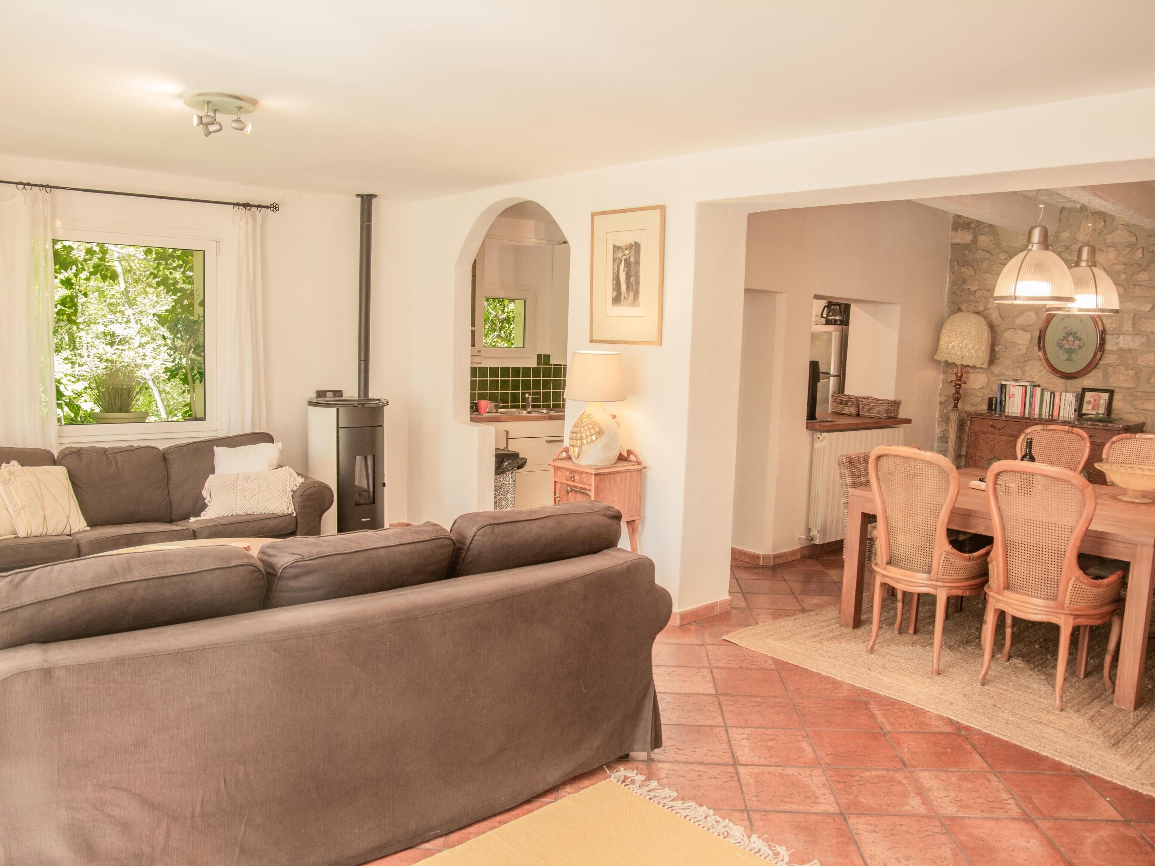 Ein Wohnzimmer mit einer Couch, einem Kamin, einem Essbereich mit Korbstühlen und einer durch einen Bogen sichtbaren Küche.