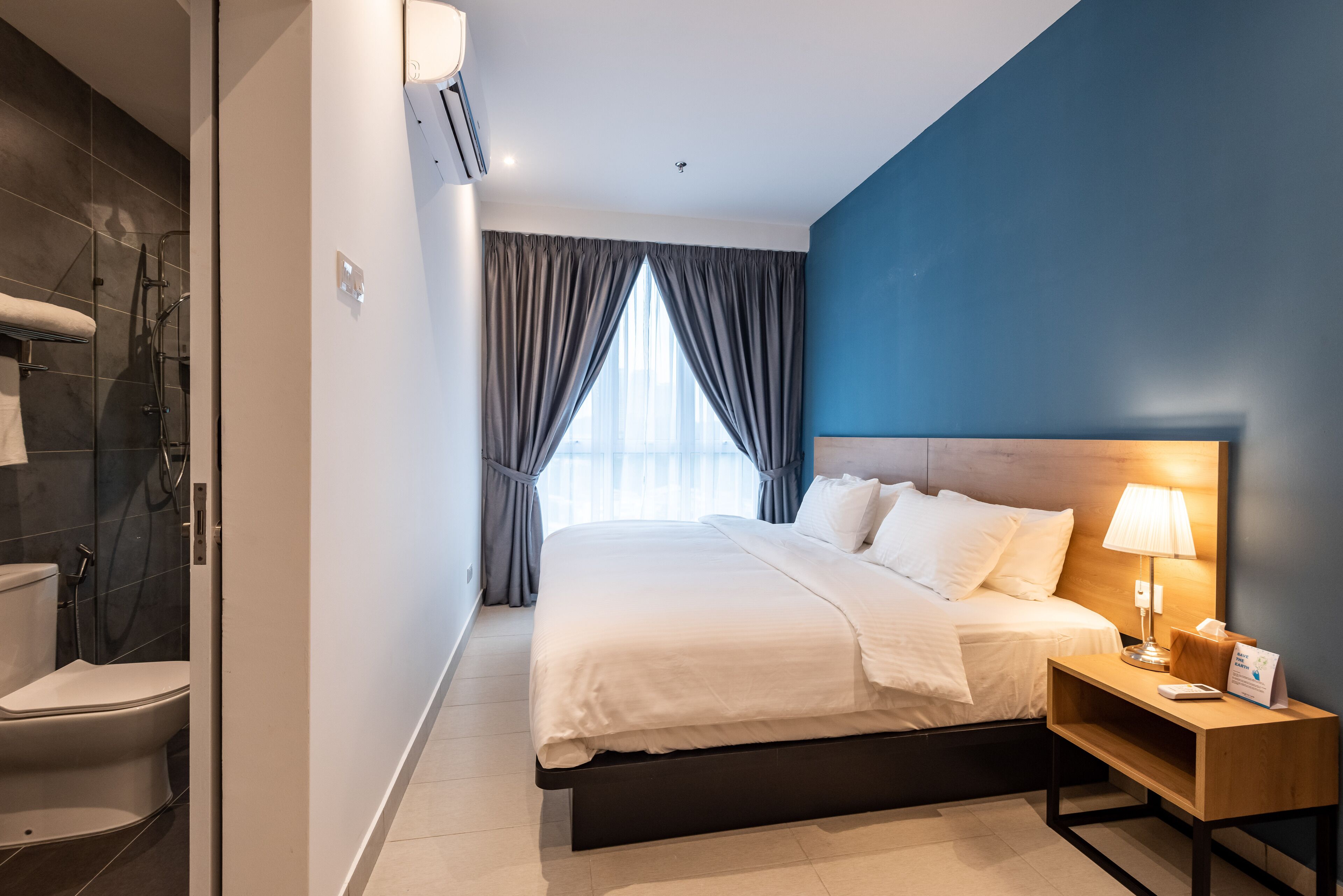 Een moderne hotelkamer met een groot bed, een nachtkastje met lamp, een douche en uitzicht op de stad door het raam.