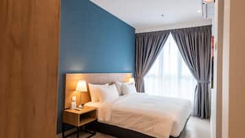 Quarto de hotel com uma cama grande, cabeceira de madeira, mesa de cabeceira com abajur e vista para o exterior através de grandes janelas com cortinas.