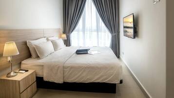 A hotel room with a bed, bedside table, lamp, and a TV on the wall.