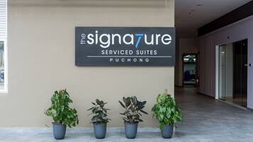 A reception area with a sign for 'The Signature Serviced Suites' in Puchong. There are three potted plants in front of the sign.