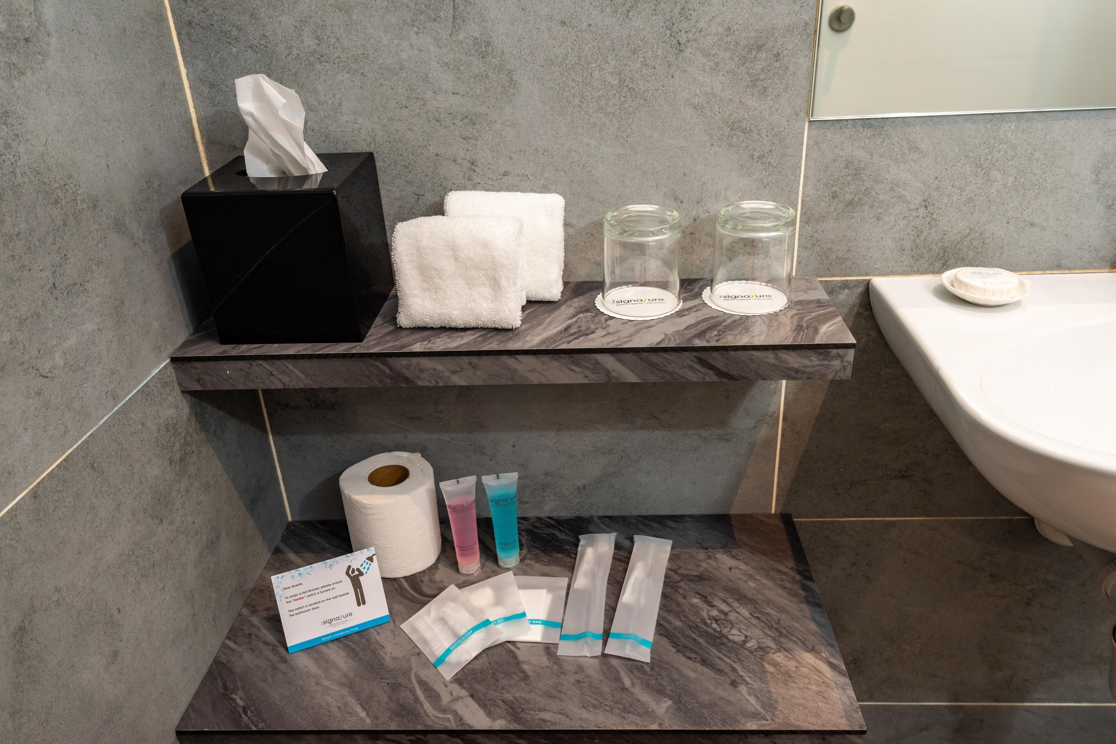 A bathroom with a marble shelf holding a tissue box, towels, and glass jars.