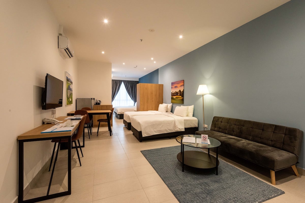 A hotel room with a bed, a sofa, a desk with a chair, a television, and a lamp.