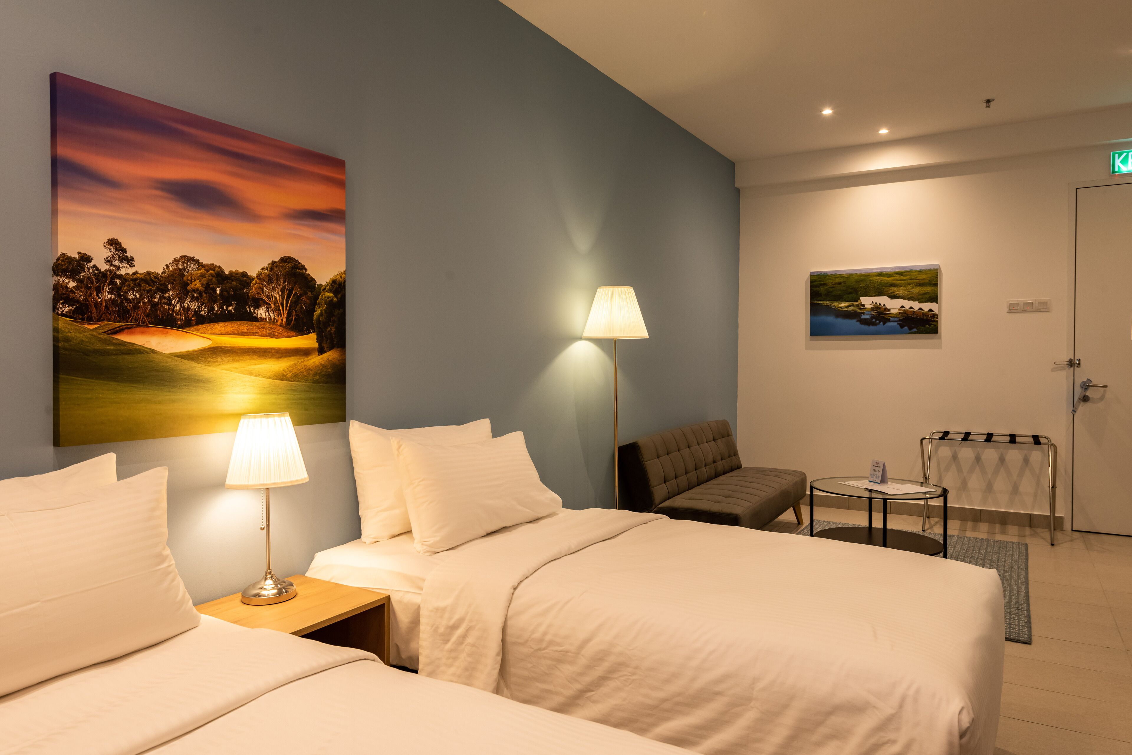 Une chambre d’hôtel avec deux lits, un bureau, une chaise, une lampe et un tableau au mur.