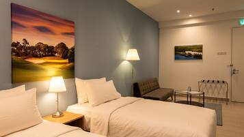 Une chambre d’hôtel avec deux lits, un bureau, une chaise, une lampe et un tableau au mur.