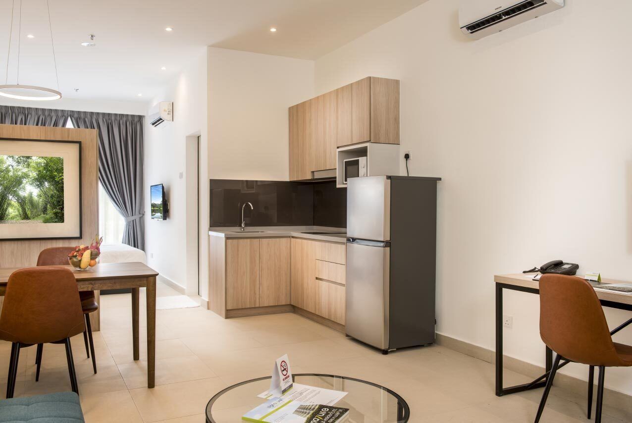 Cocina moderna con armarios de madera, un refrigerador de acero inoxidable y un microondas. Cuenta con un comedor con mesa y sillas, y una pequeña mesa redonda con cubierta de vidrio.