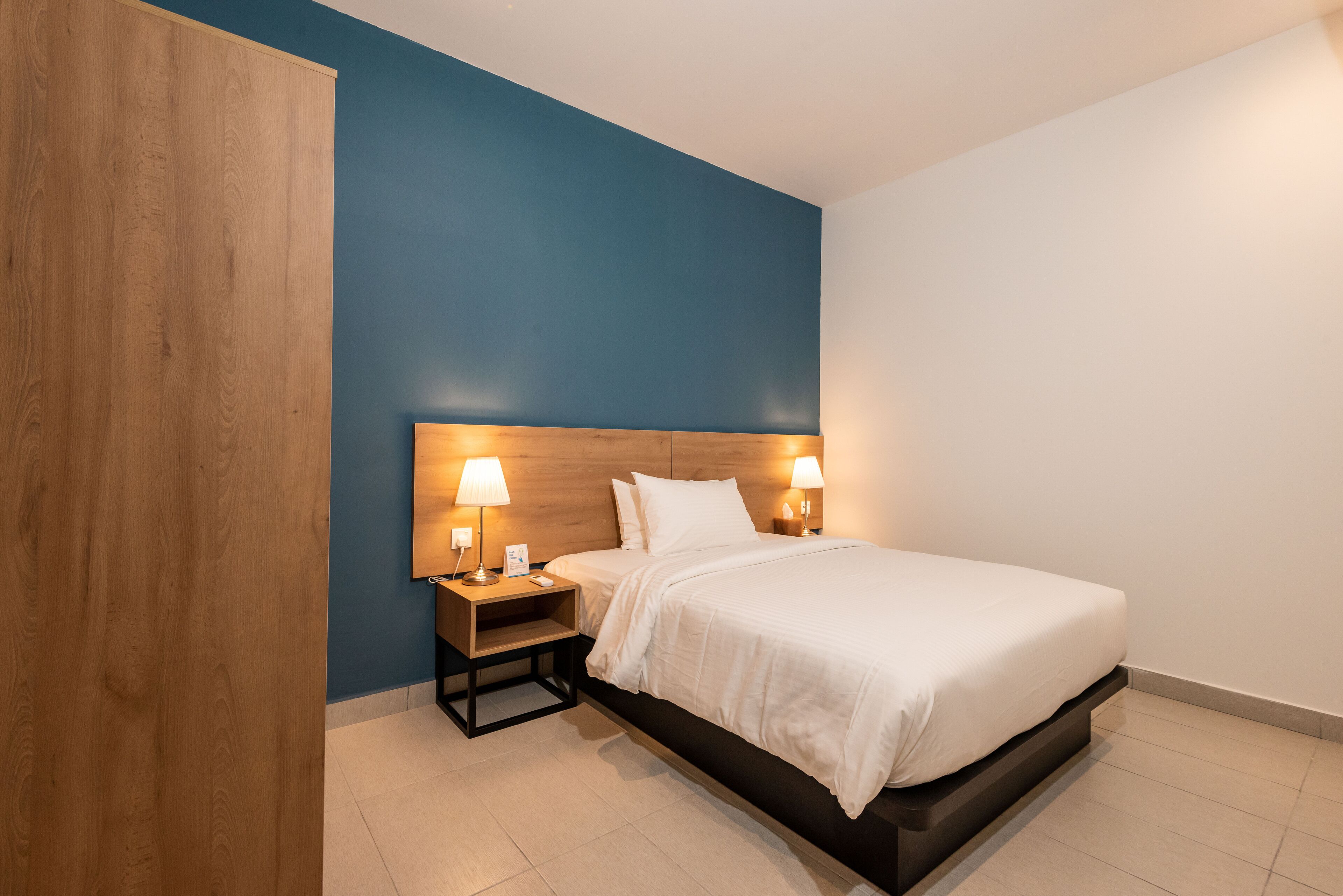 A modern hotel room with a bed, nightstands, and wall-mounted lamps.