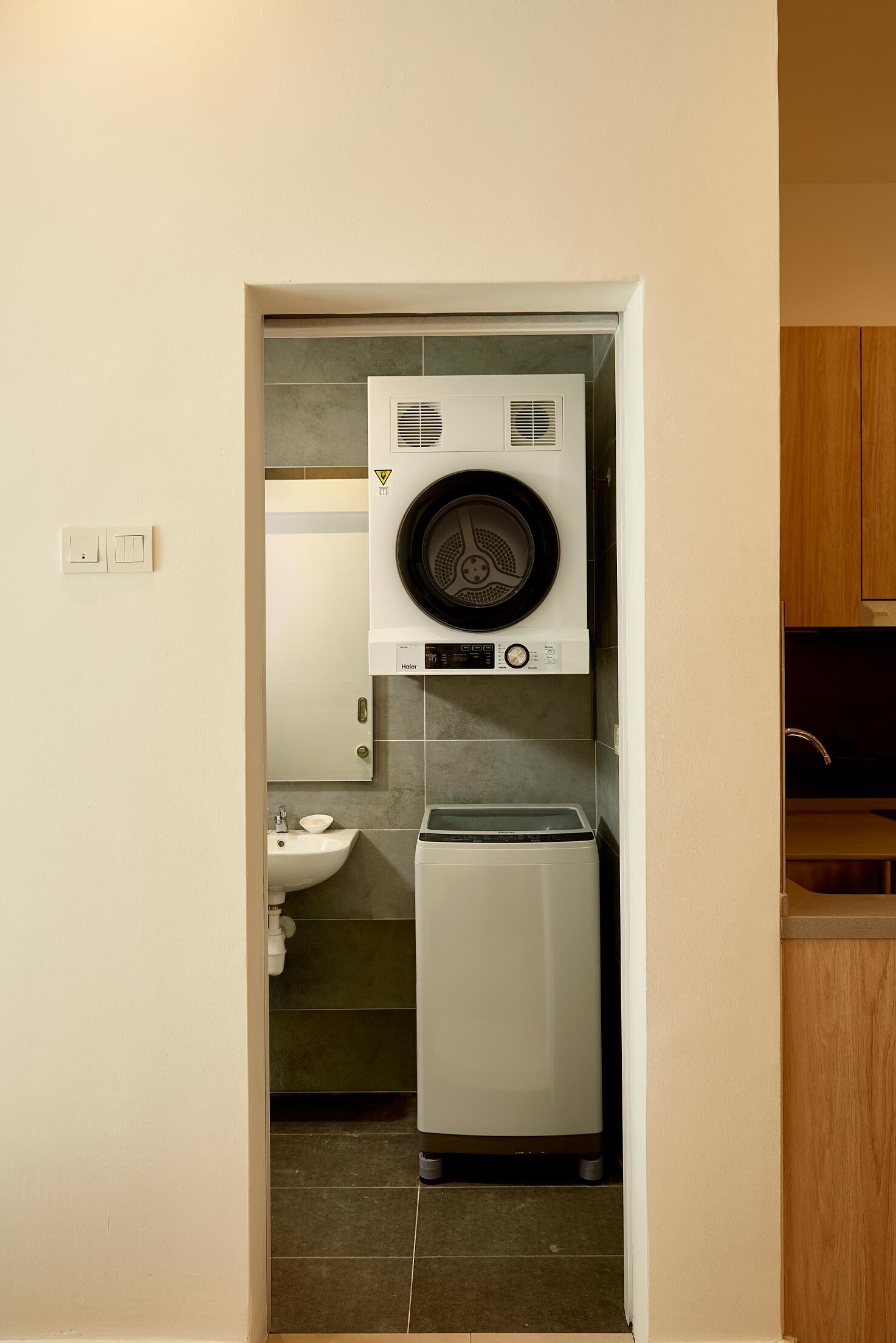 A compact laundry room with a front-loading washer and dryer, a sink, and a mirror above the dryer.