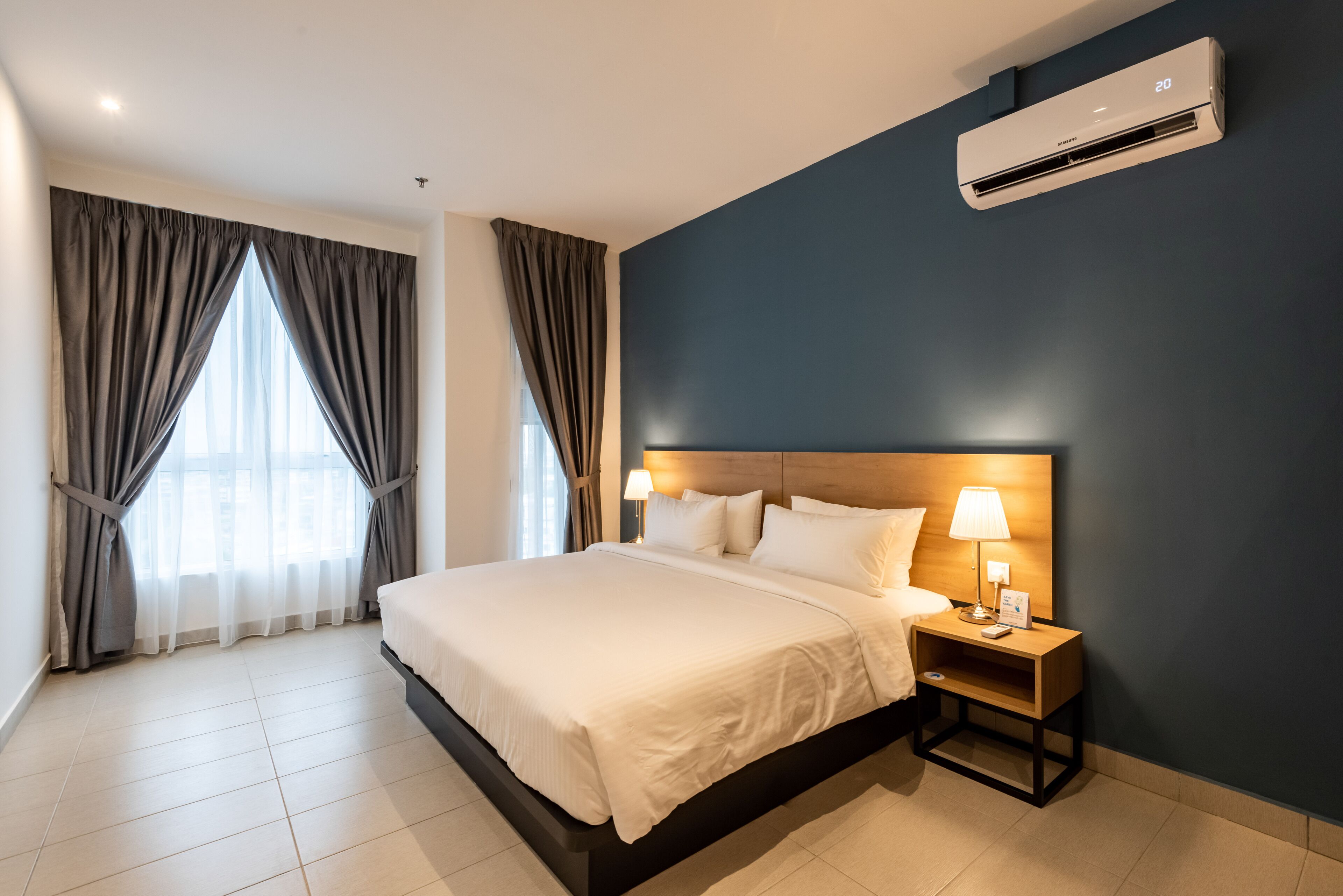 A hotel room with a large bed, a nightstand with a lamp, and an air conditioning unit on the wall.