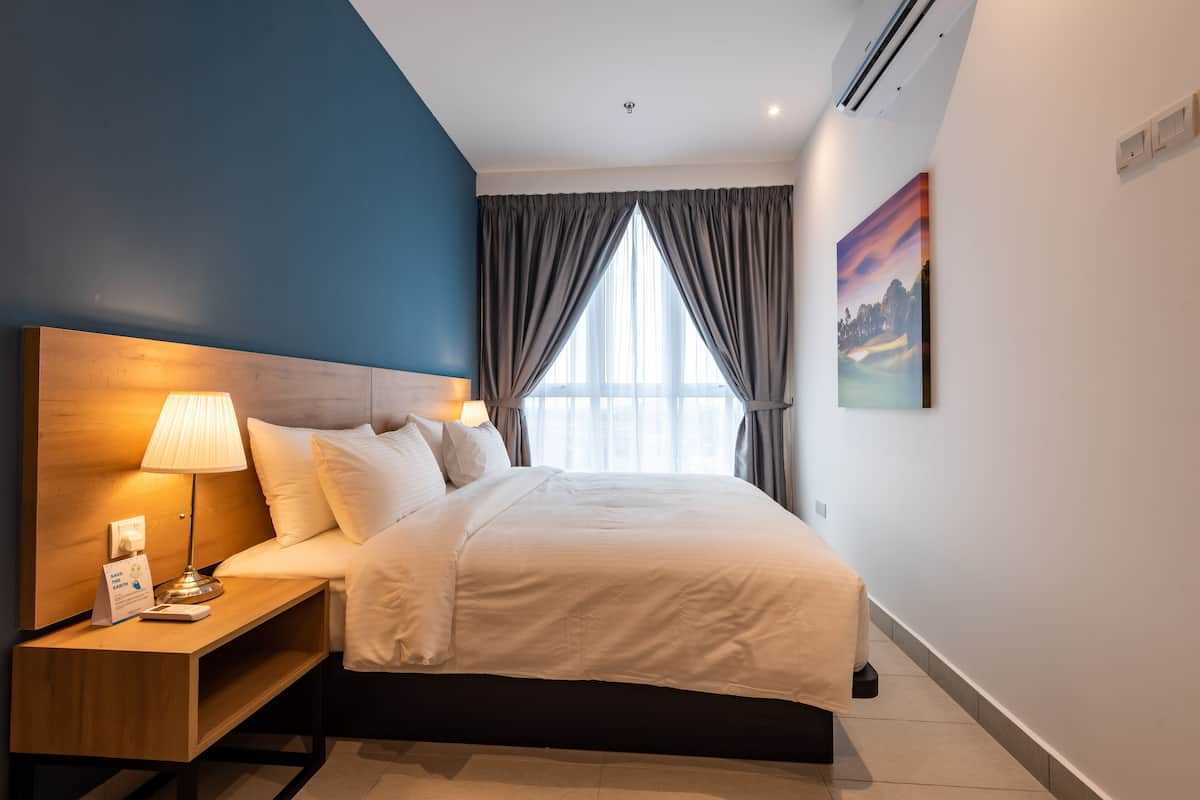 A modern hotel room with a large bed, a bedside table with a lamp, a nightstand, and a painting on the wall.