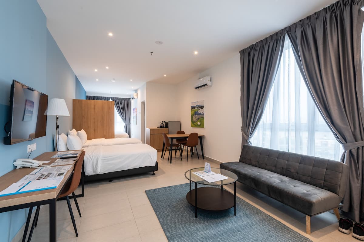 A hotel room with a bed, a sofa, a desk with a chair, a small table, and a TV on the wall.