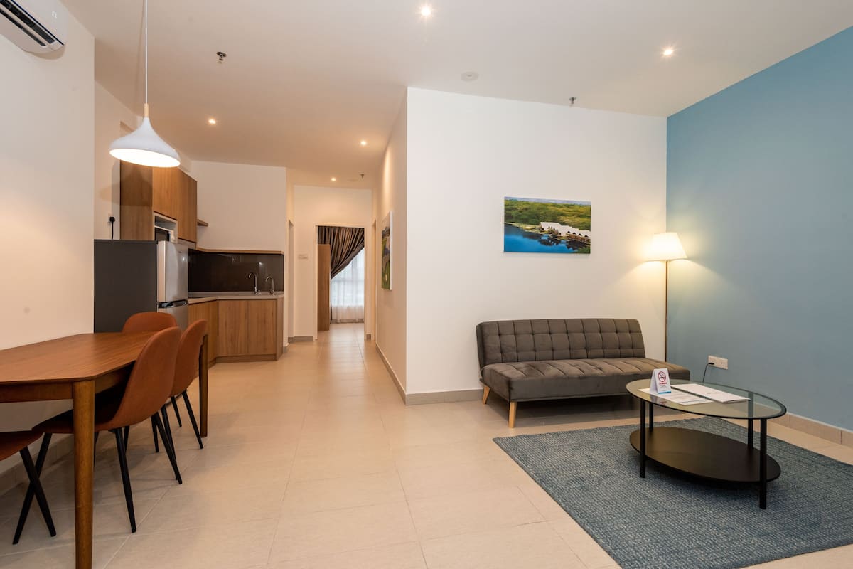 A modern living room with a sofa, a dining table with chairs, a kitchen area, and a painting on the wall.