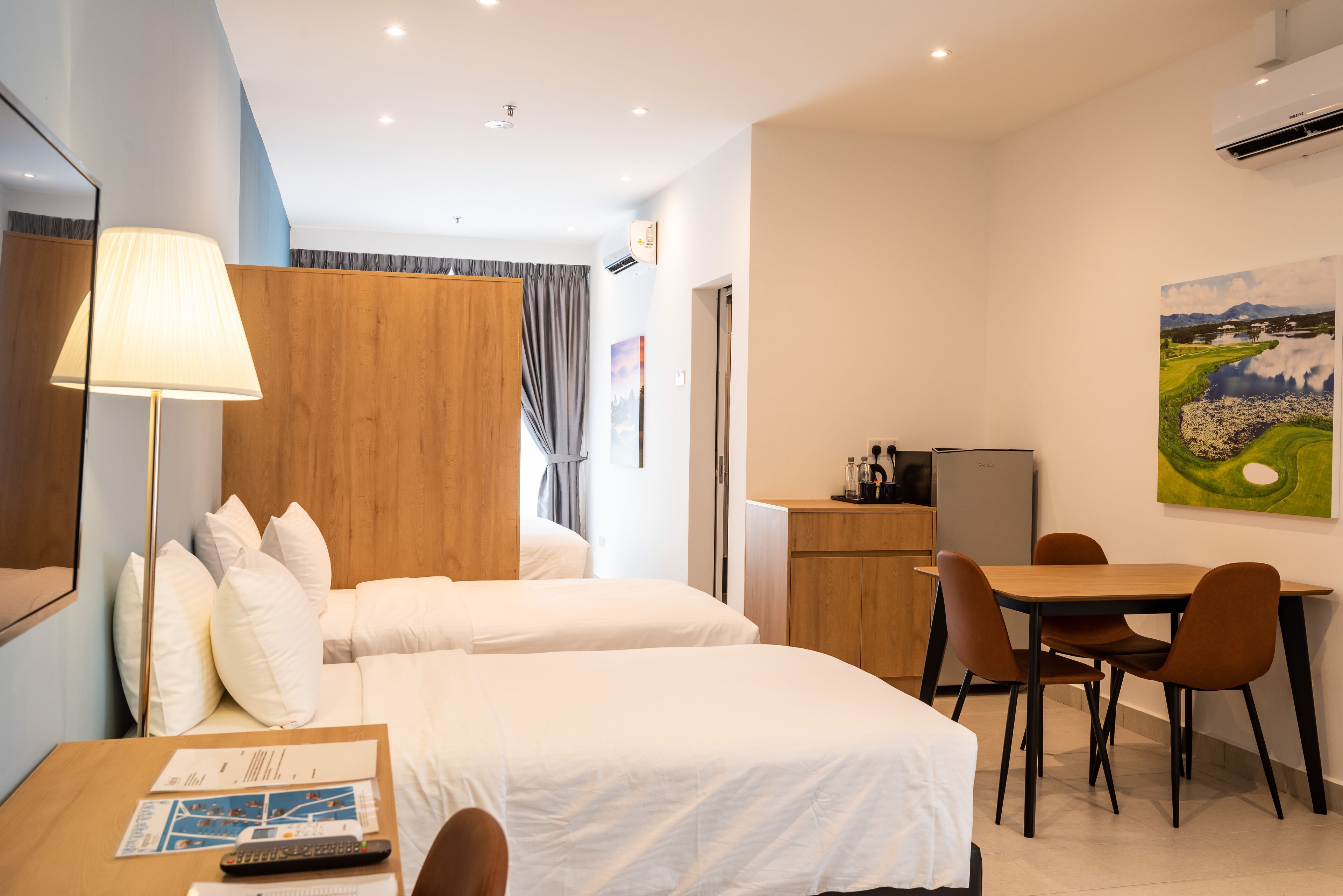 Ett hotellrum med två sängar, ett skrivbord med en lampa, en matplats med stolar, ett kylskåp och en tavla på väggen.