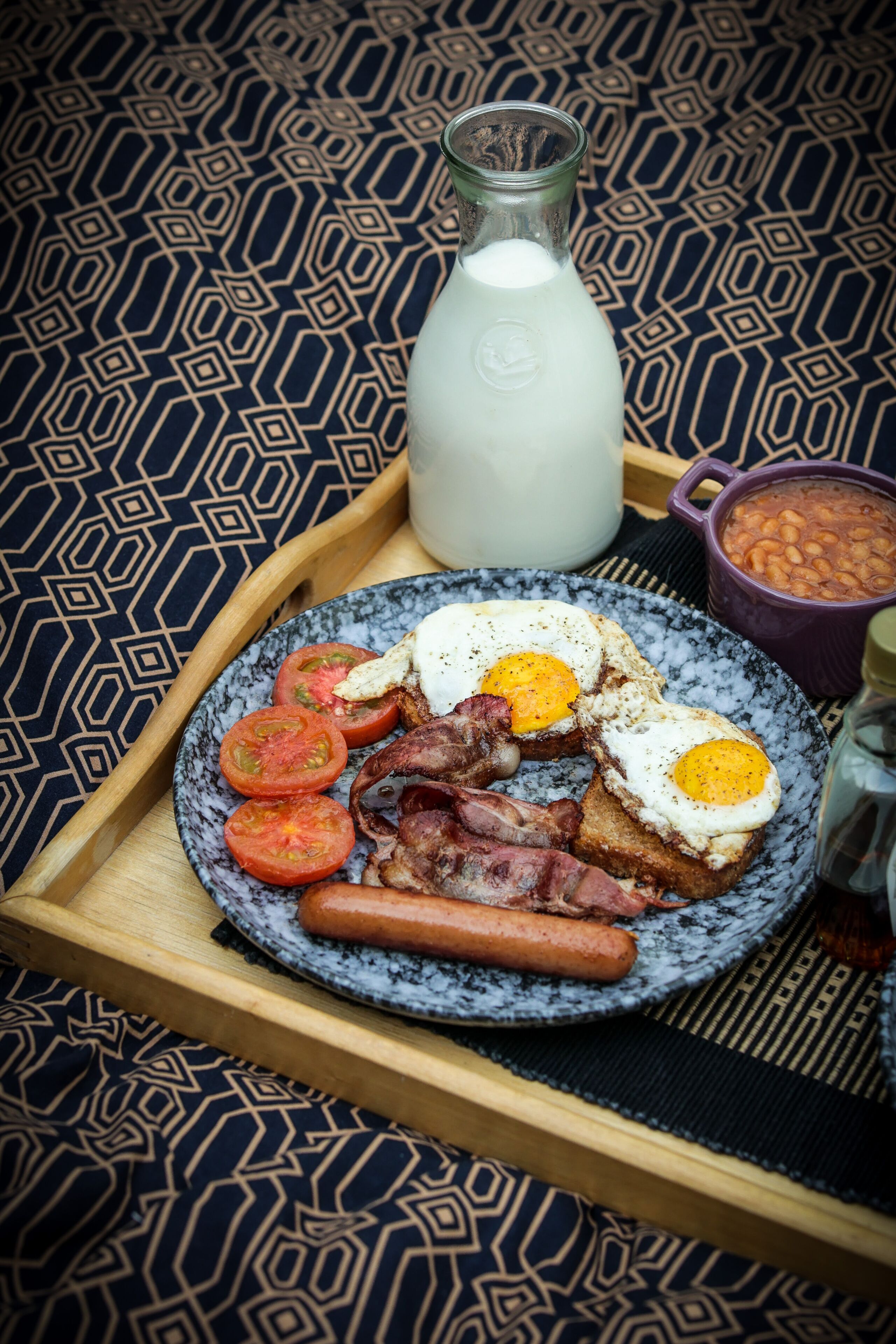 Ein Frühstücksbrett mit Eiern, Speck, Würstchen, Tomaten und Toast.