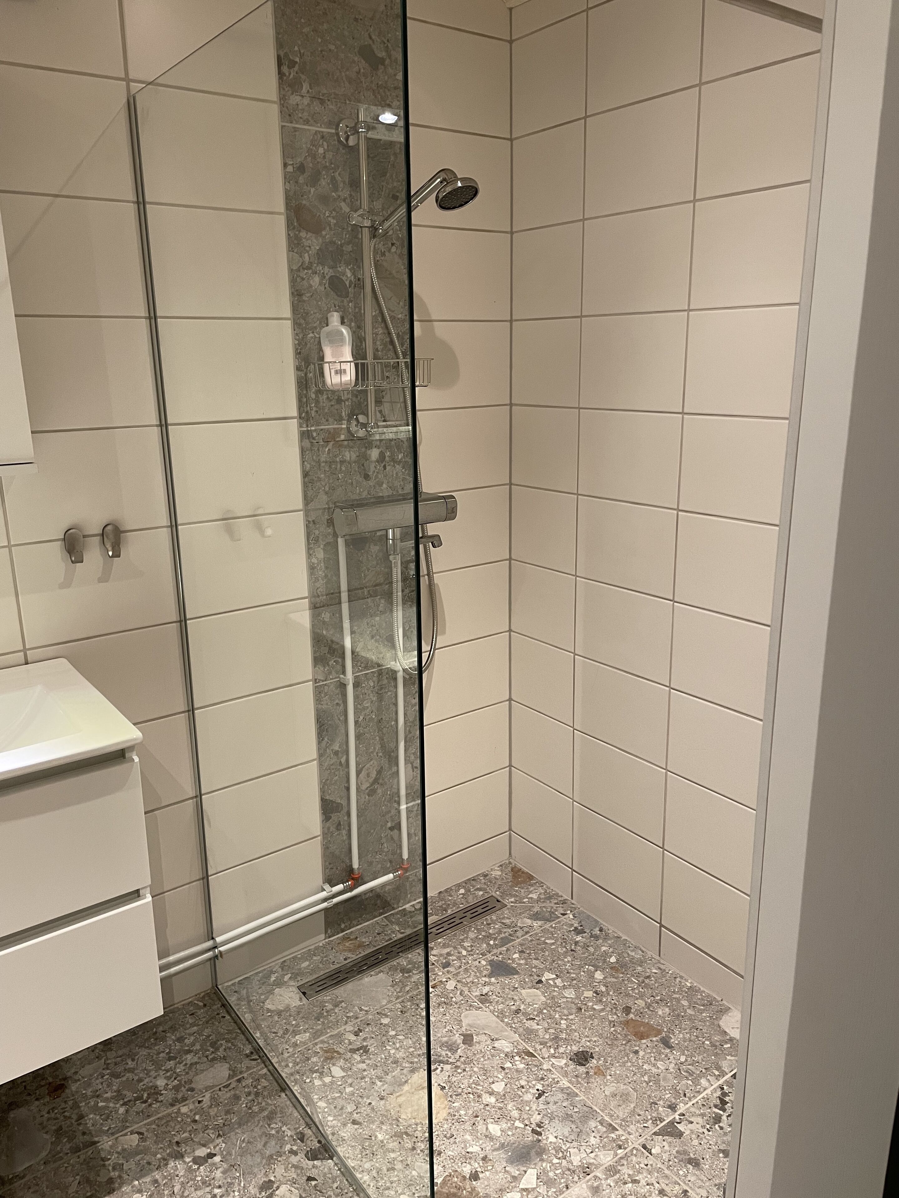 A glass-enclosed shower with a marble floor, a white sink, and a towel rack.