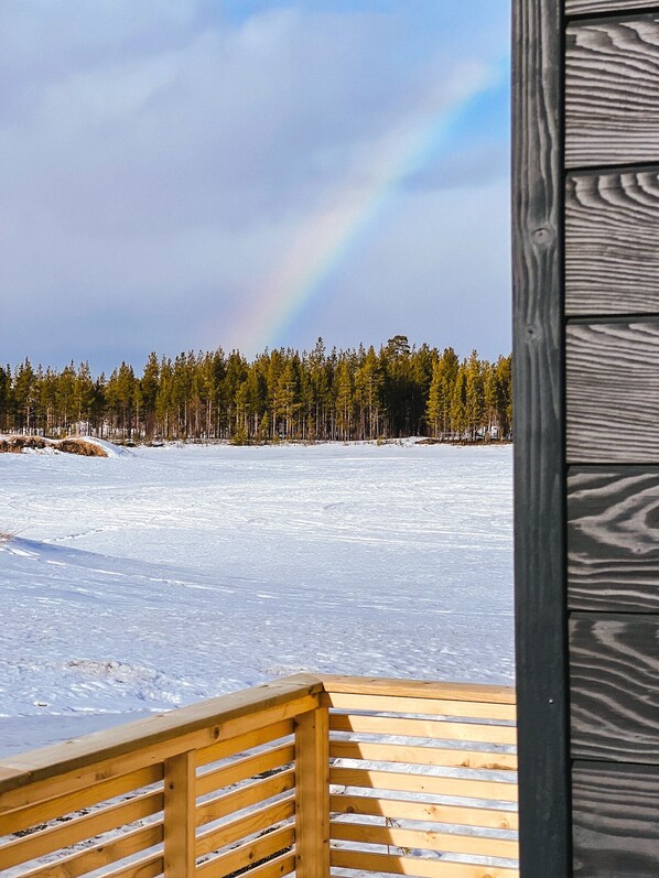 A wooden deck overlooking a snowy landscape with a forest and a rainbow.