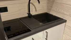 Una cocina moderna con encimera negra, pileta negra, estufa integrada y muebles de color blanco.