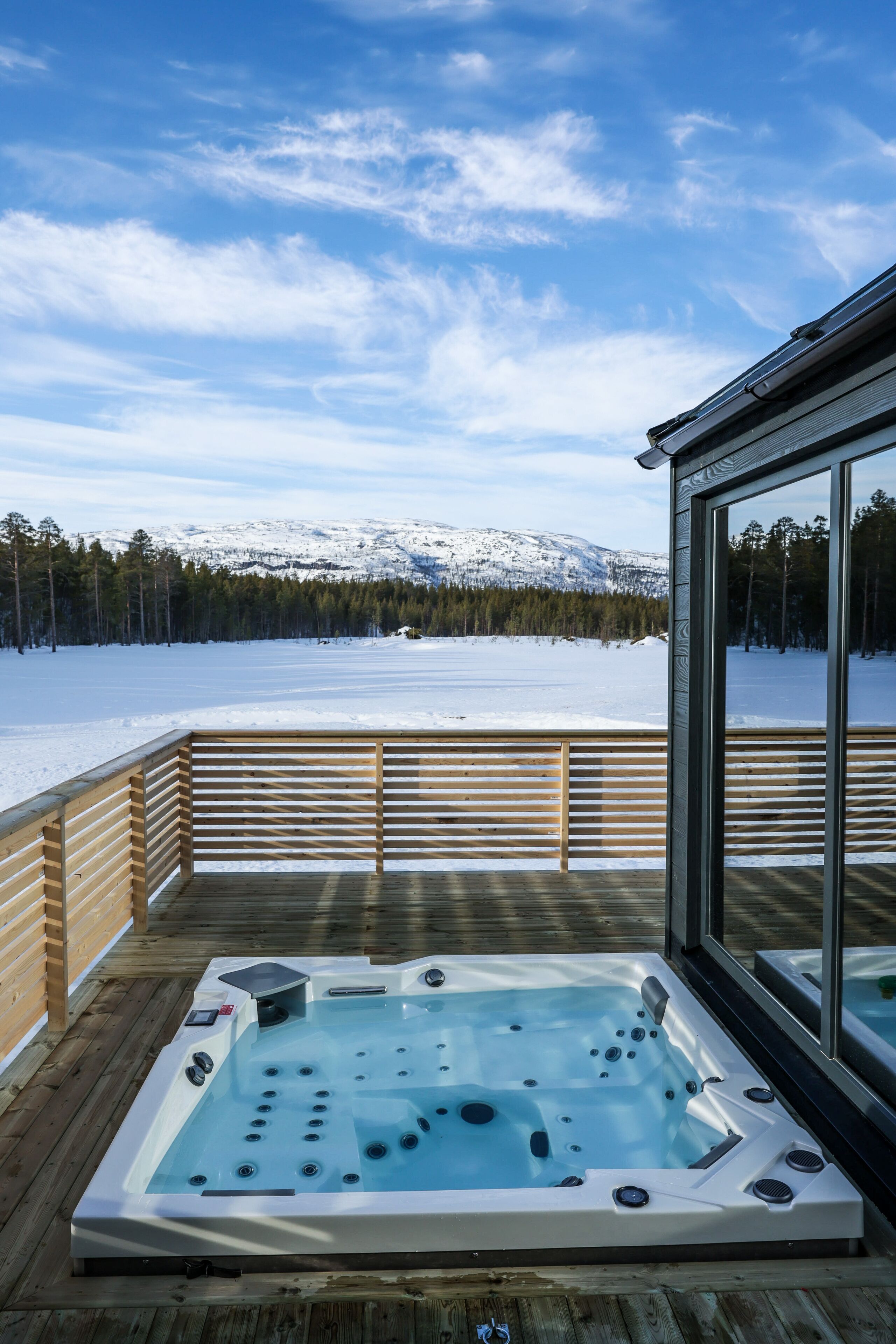 Een hottub op een houten terras, met een besneeerd landschap en bergen op de achtergrond.