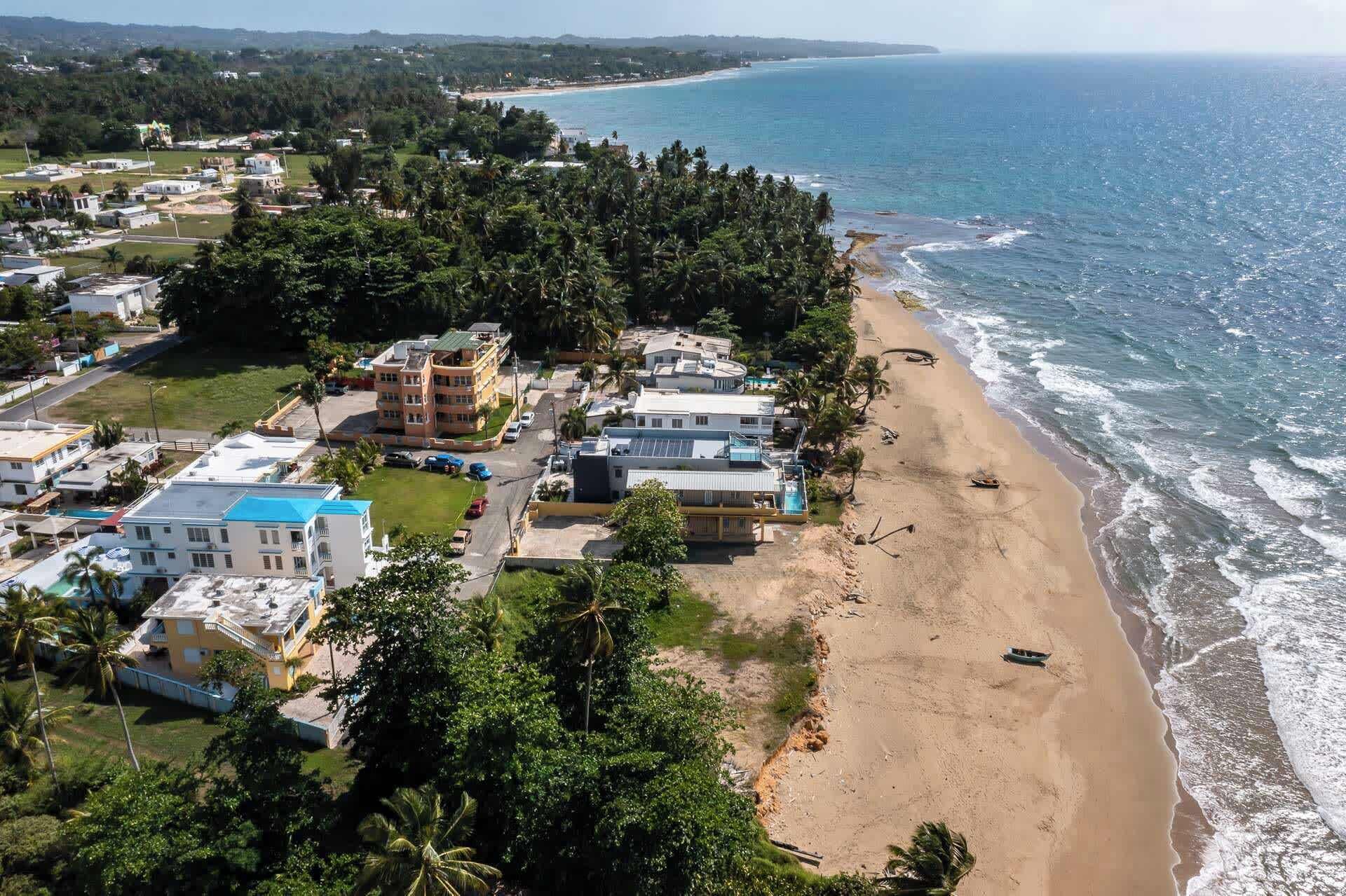 Zona residencial costera con propiedades frente al mar, incluyendo edificios de varios pisos y casas de un piso, rodeada de densa vegetación tropical.